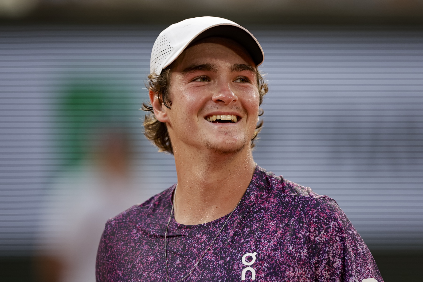 João Fonseca smiling on court in a white cap